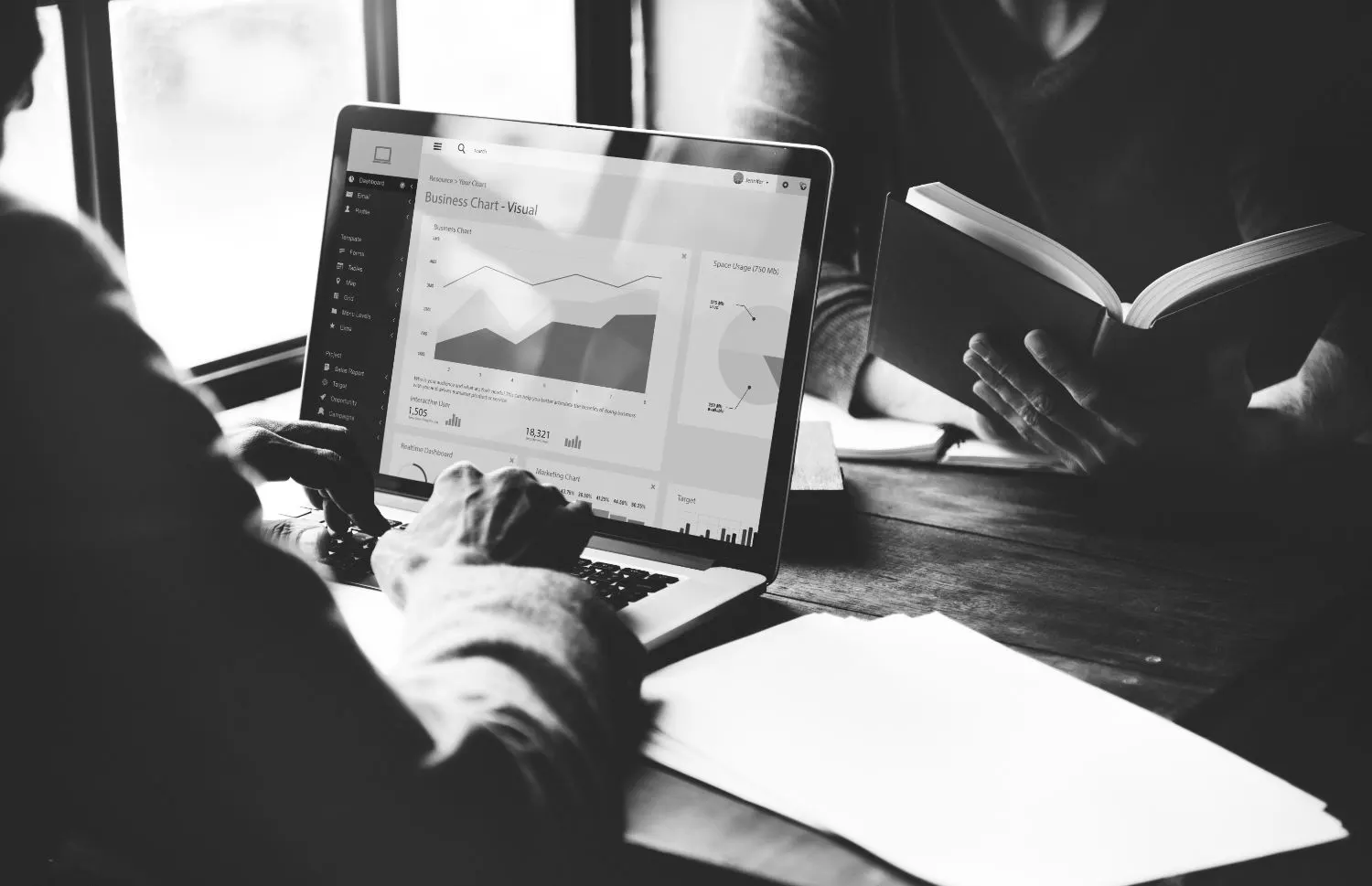 Colegas trabajando con un portátil que muestra gráficos de negocio, en blanco y negro