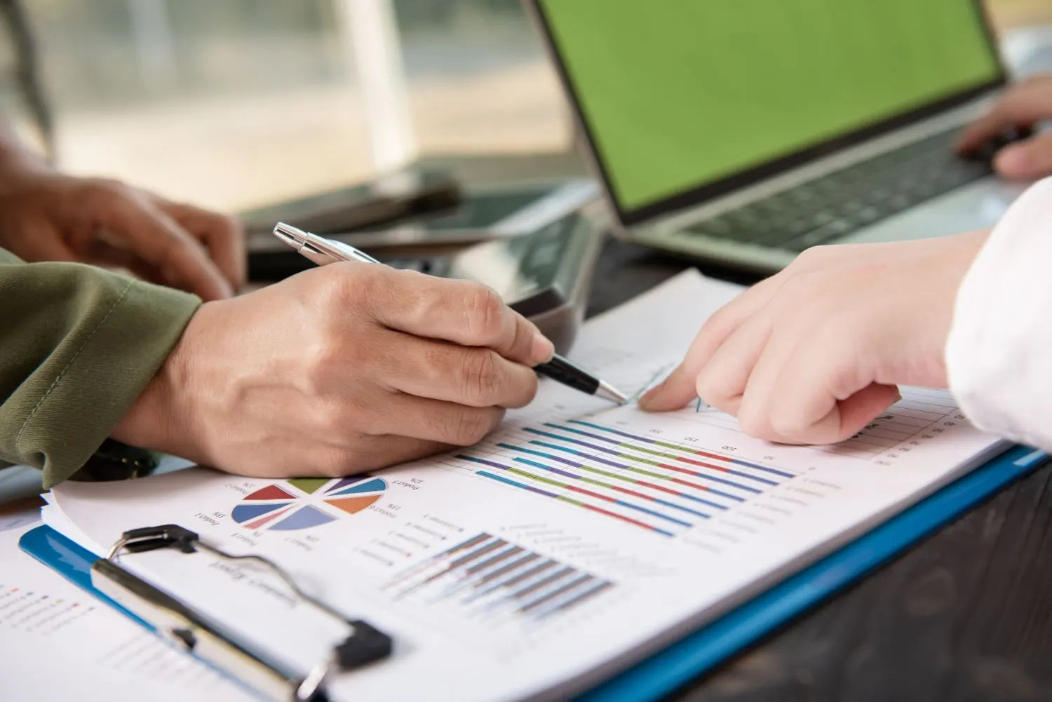 Dos personas revisan un informe impreso con gráficos junto a un portátil