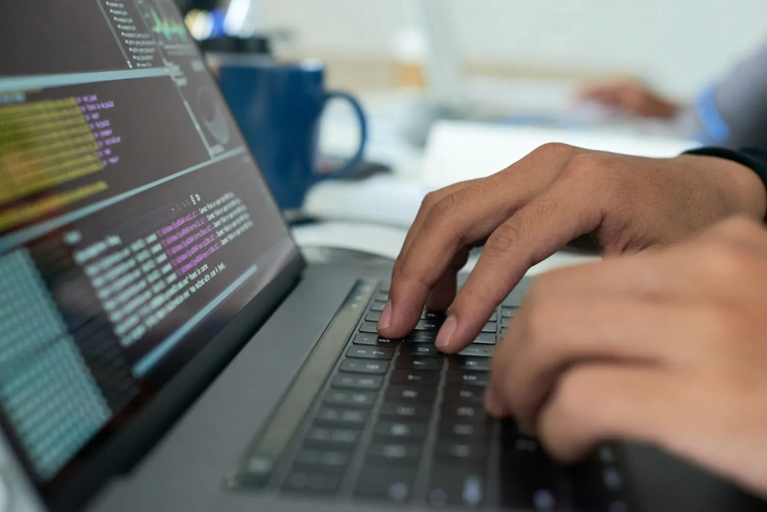 Manos tecleando en un portátil con código en la pantalla