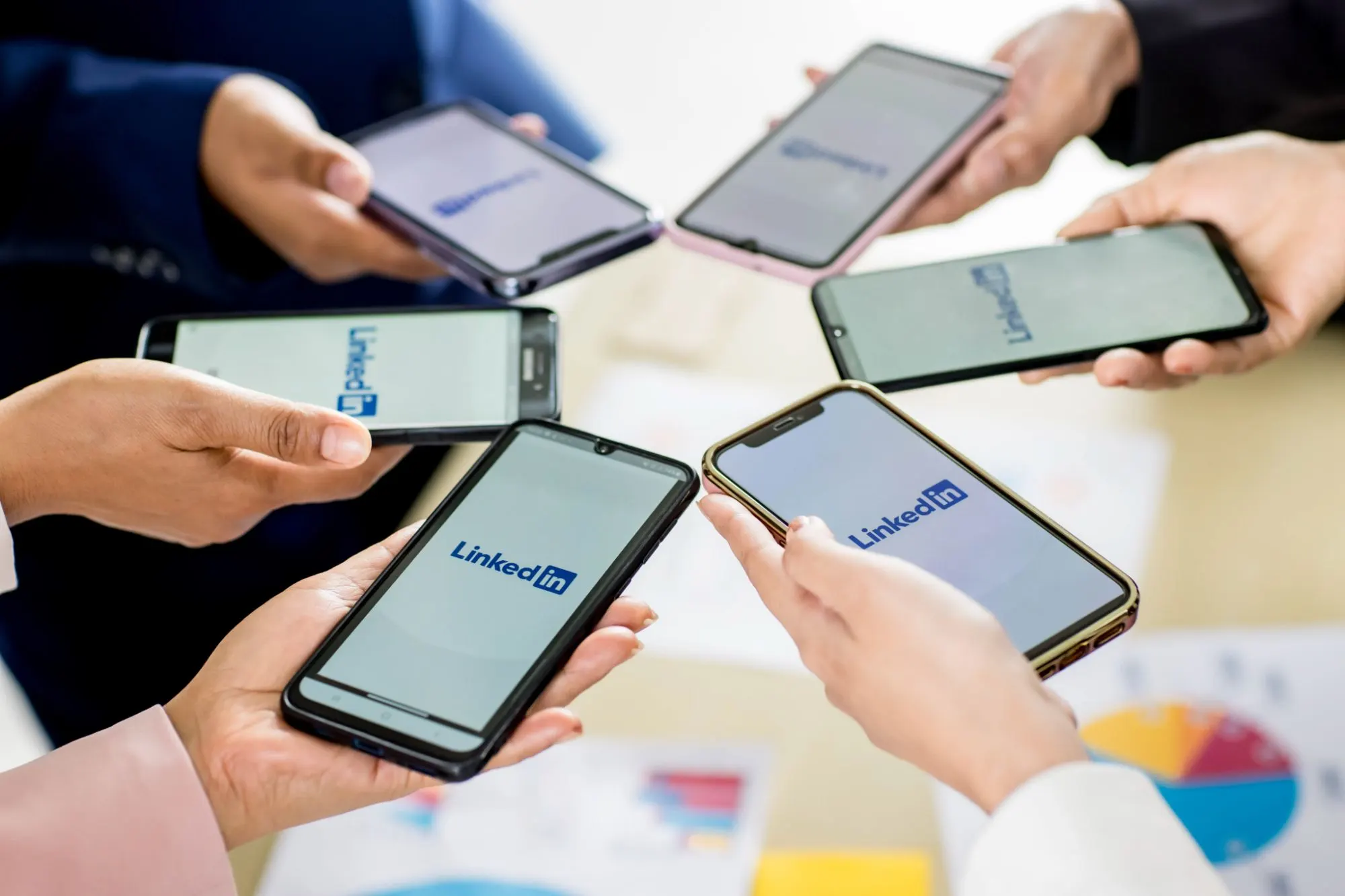 Varias manos en círculo sostienen móviles con la aplicación de LinkedIn abierta