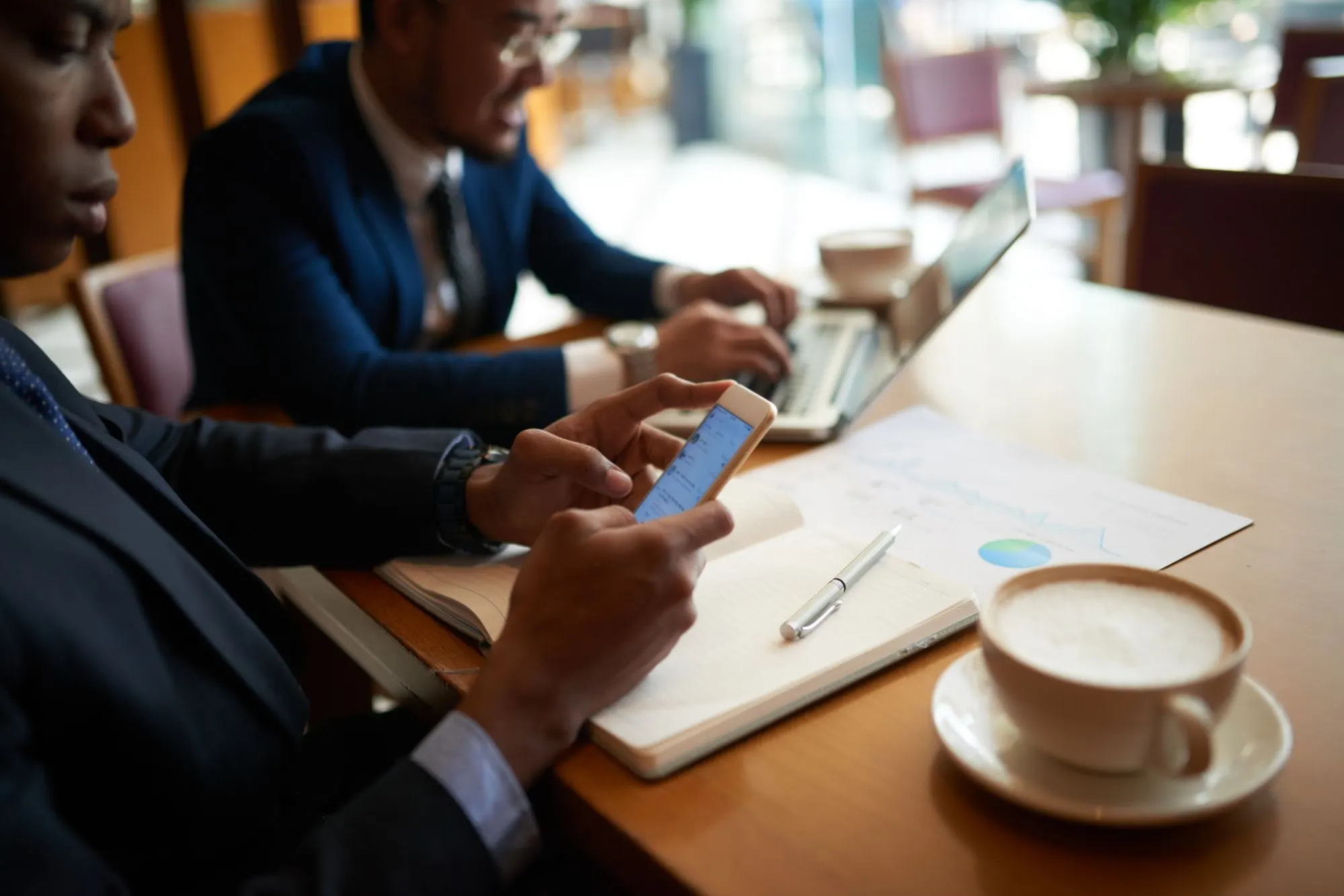 Hombres de negocios en una cafetería, uno con el móvil y otro con el portátil