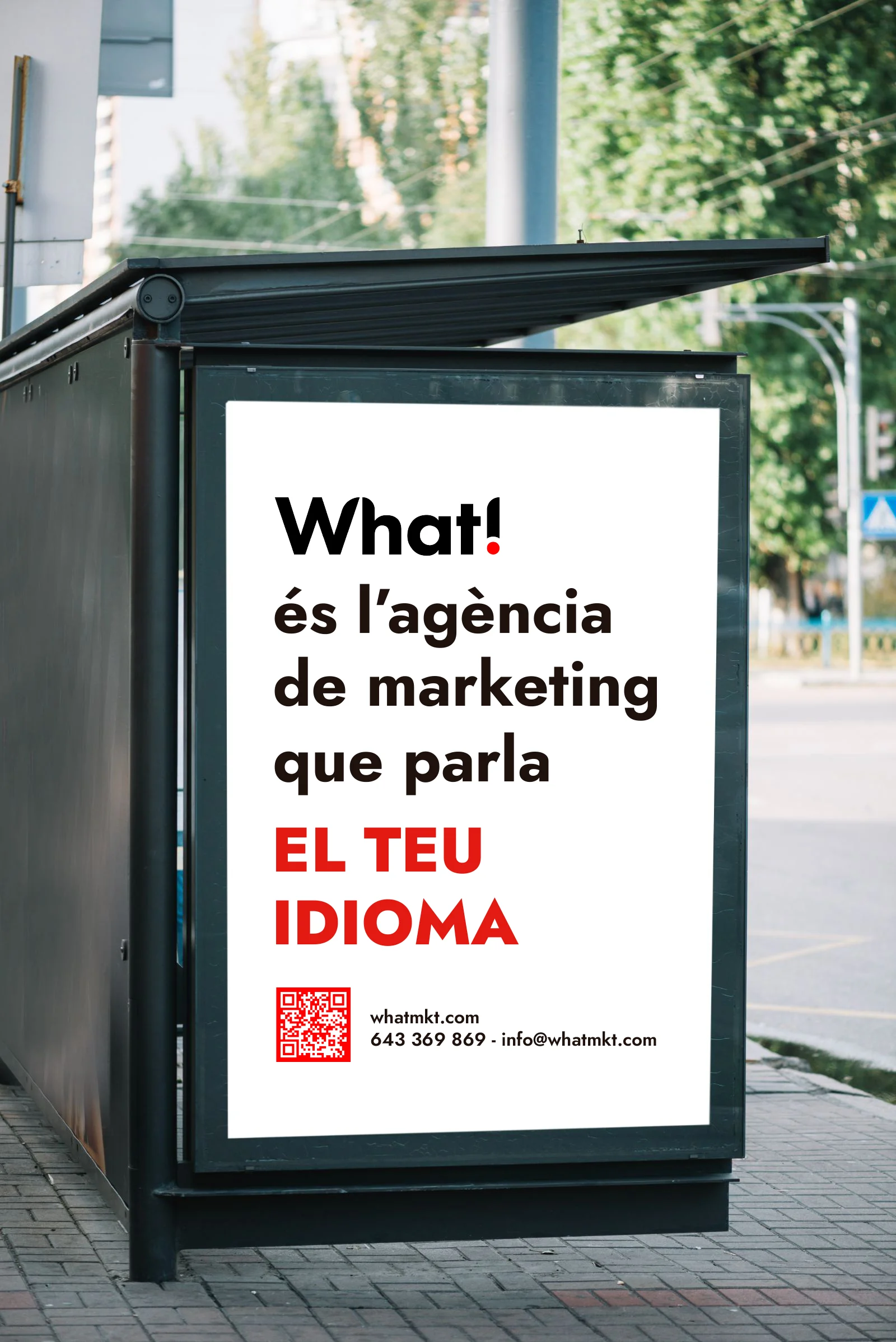 Marquesina de autobús con un cartel de What!: «és l'agència de marketing que parla el teu idioma»