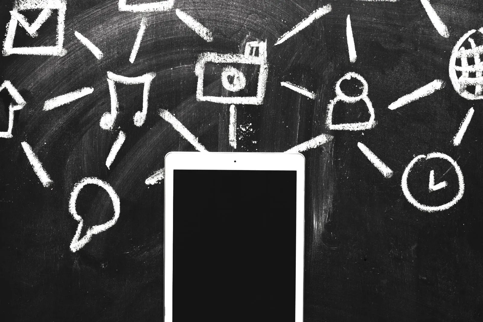 Tableta sobre una pizarra con iconos dibujados con tiza conectados entre sí