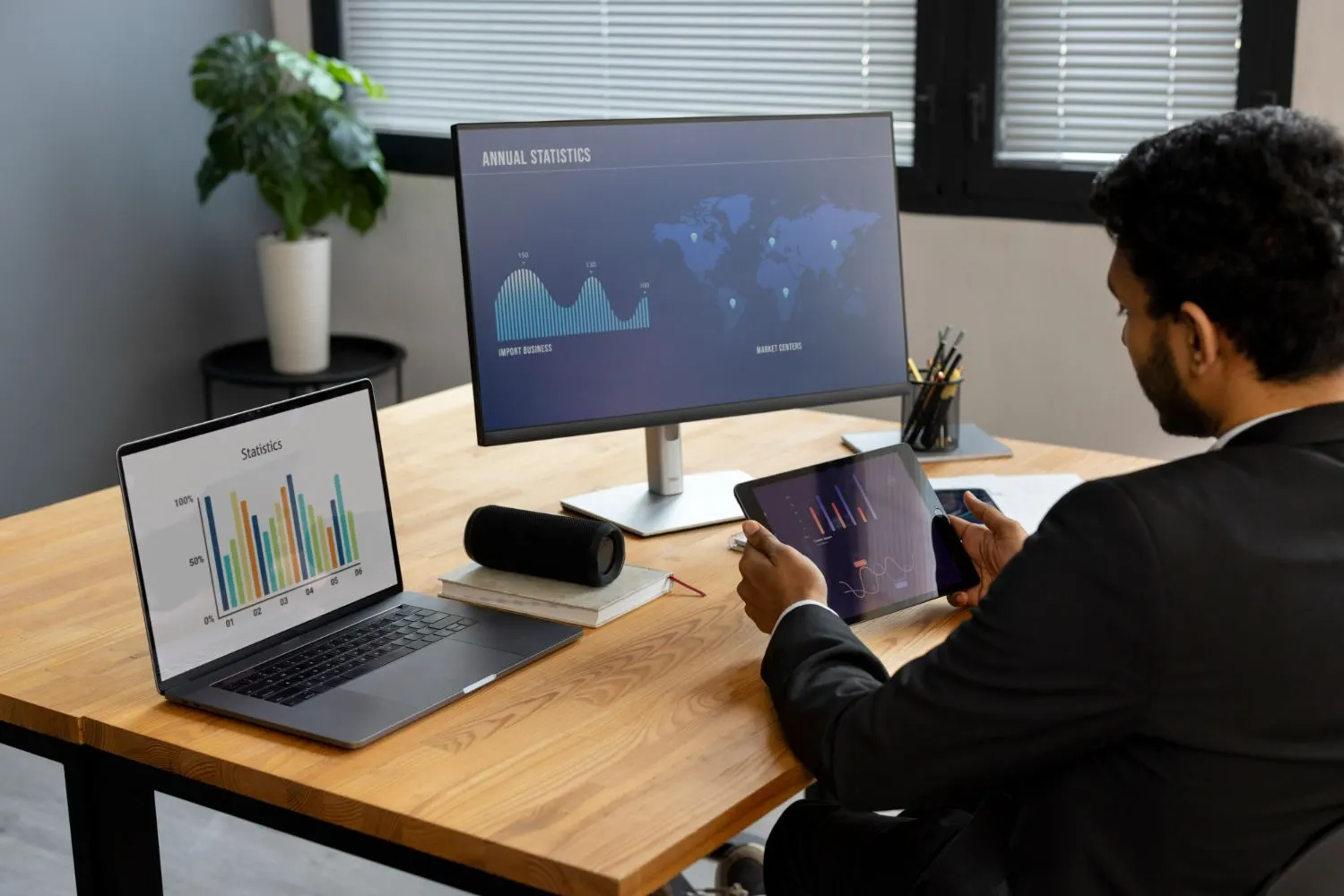 Hombre revisando gráficos en una tableta frente a un monitor y un portátil con estadísticas