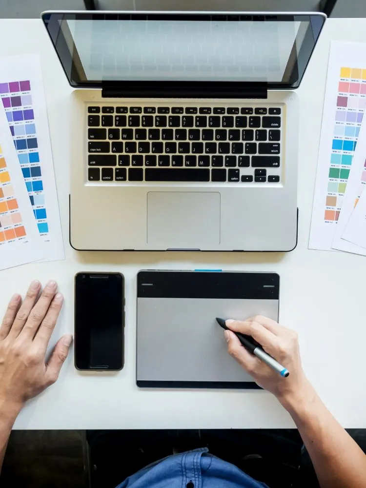 Vista cenital de un diseñador con tableta gráfica, portátil y cartas de colores