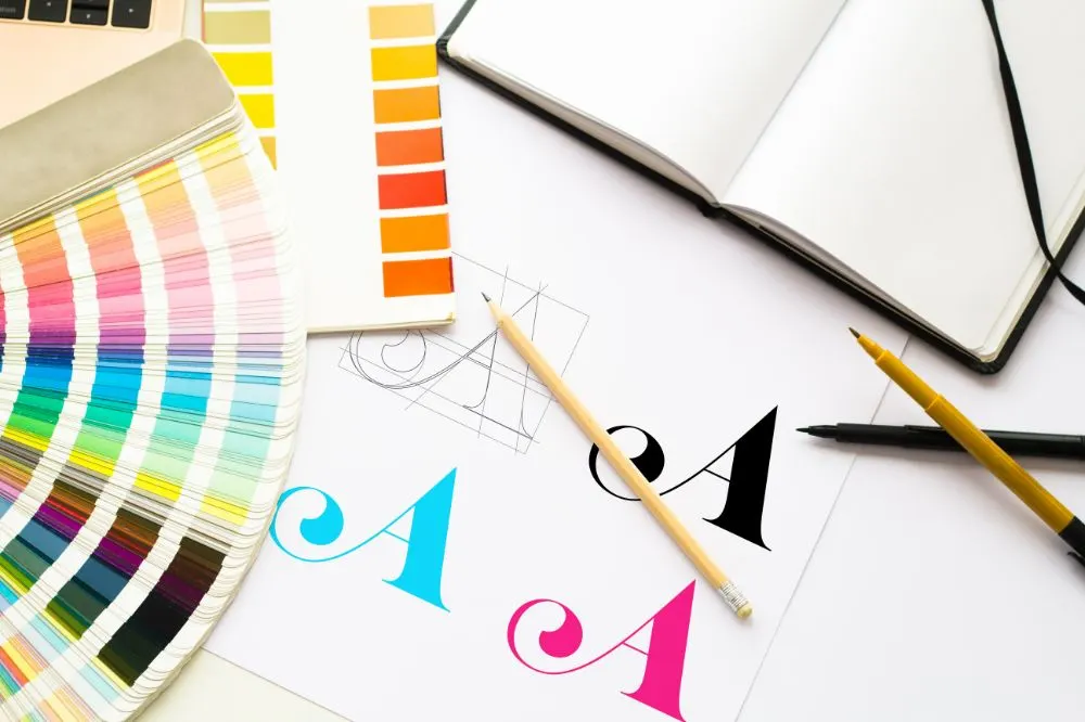 Muestrario de colores Pantone y bocetos de una letra A en varios colores sobre la mesa