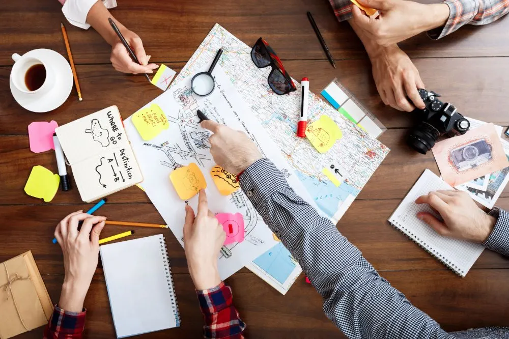 Equipo trabajando sobre un mapa con notas adhesivas, cuadernos y una cámara en una mesa de madera