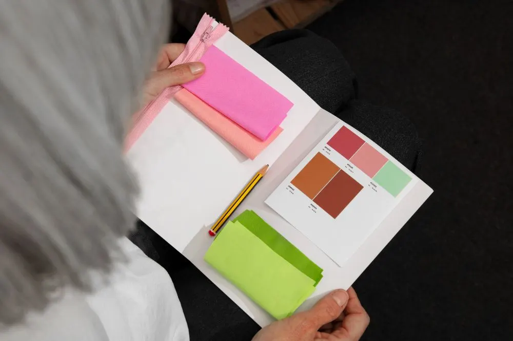Persona sosteniendo un muestrario con telas y una paleta de colores rosa, terracota y verde