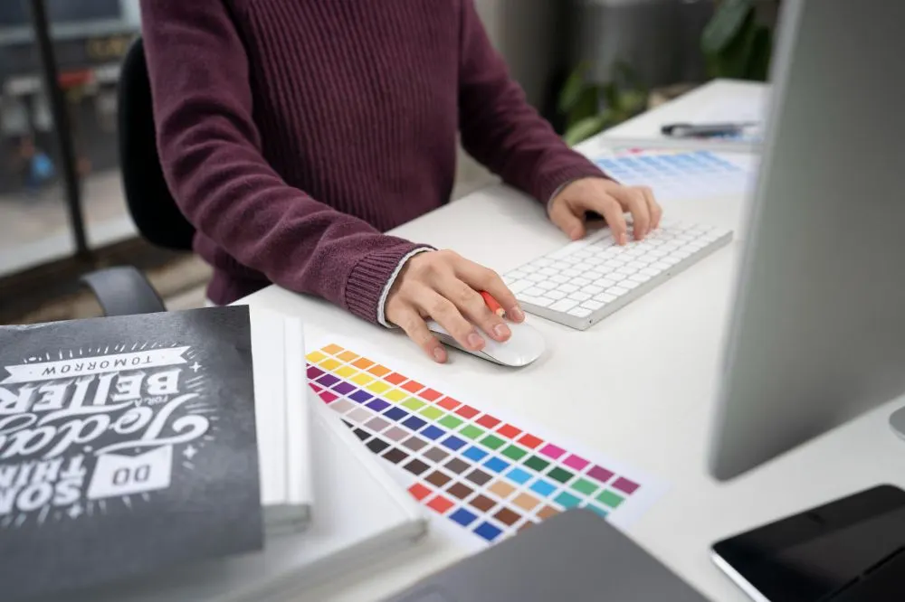 Persona trabajando con teclado y ratón junto a una carta de colores en un escritorio blanco