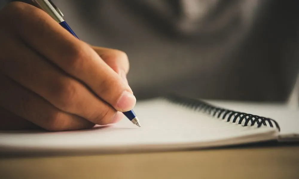 Mano escribiendo con un bolígrafo en un cuaderno de espiral