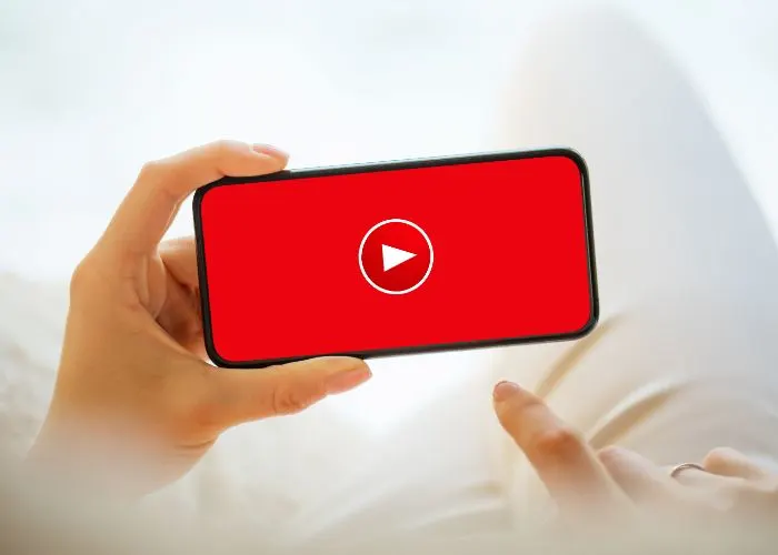 Manos sosteniendo un móvil en horizontal con un botón de reproducción rojo en pantalla