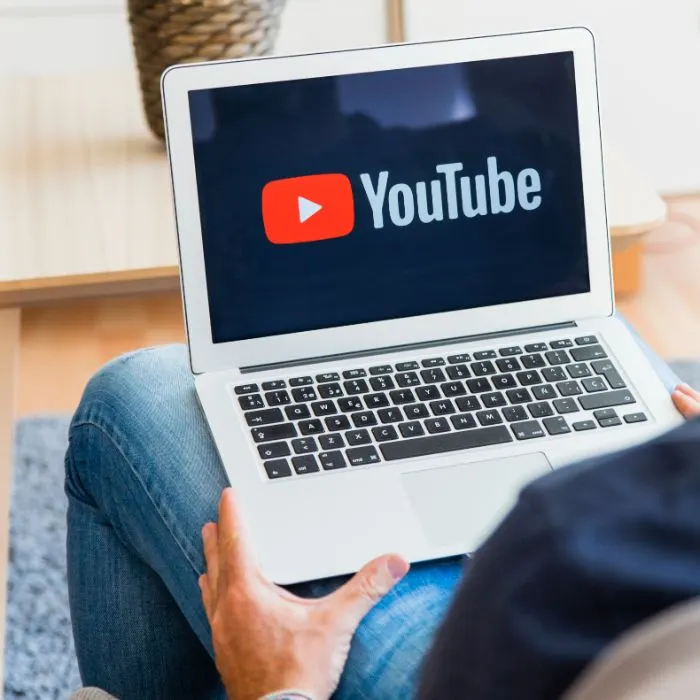 Persona con un portátil sobre las piernas que muestra el logotipo de YouTube