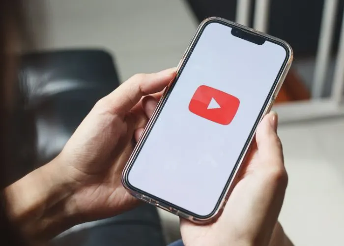 Manos sosteniendo un móvil con el logotipo de YouTube en pantalla