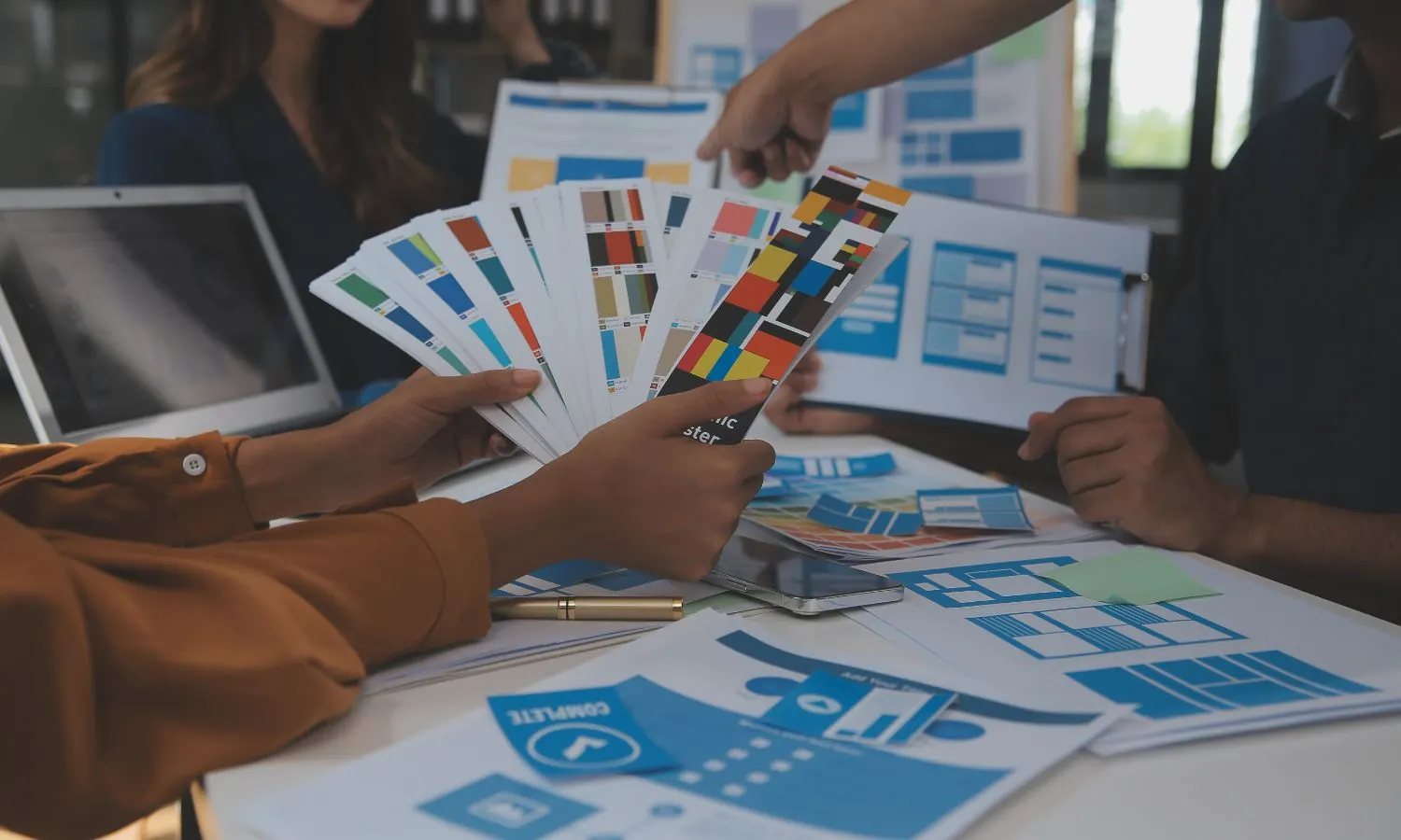 Equip de disseny revisant mostres de color i esbossos de pàgines web sobre una taula