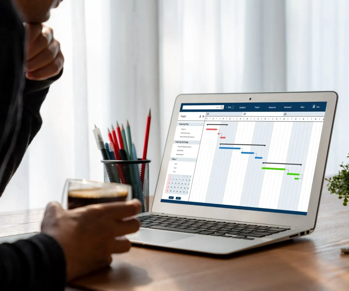Persona con un café frente a un portátil que muestra un diagrama de Gantt