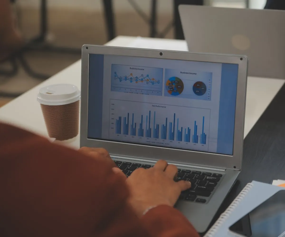 Persona tecleando en un portátil que muestra gráficos de ingresos y ventas