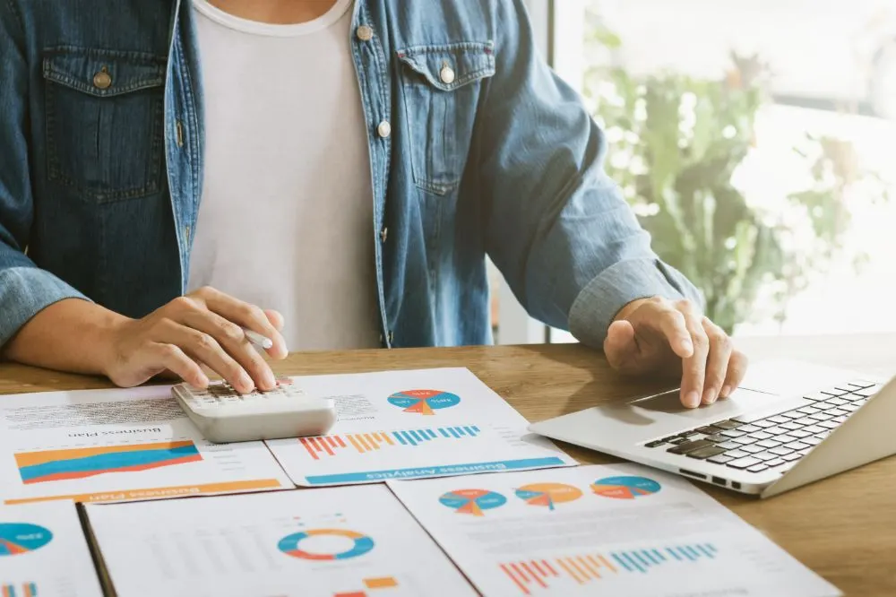 Persona con calculadora y portátil revisando informes con gráficos de negocio