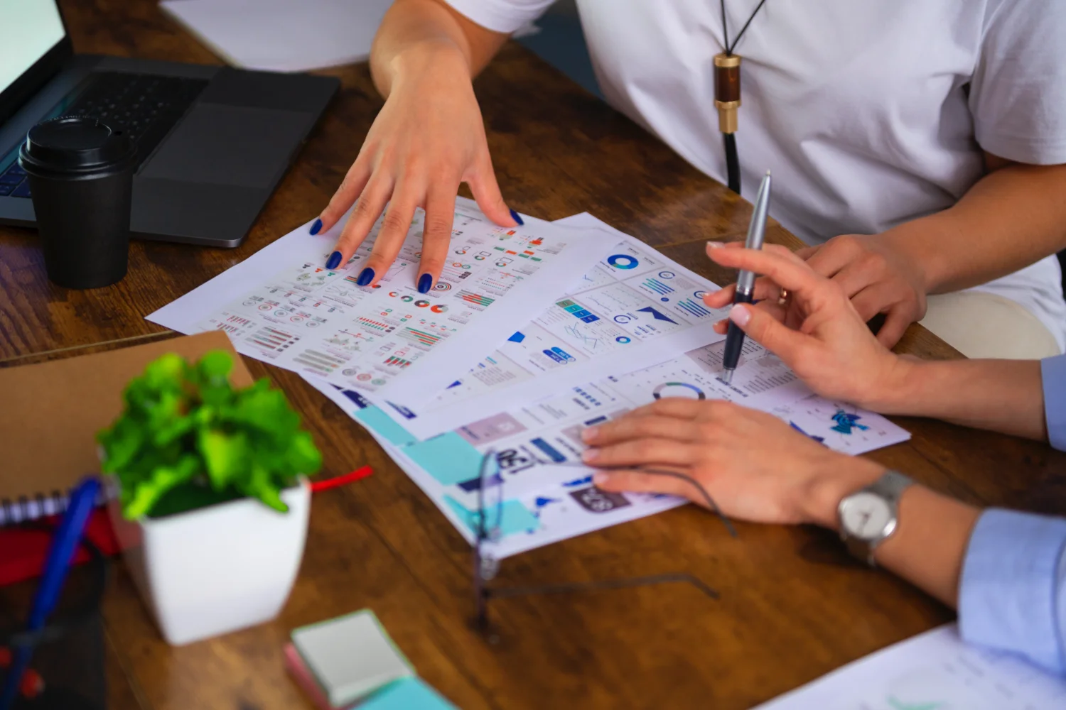 Manos de dos personas revisando hojas con gráficos e iconos sobre una mesa de madera