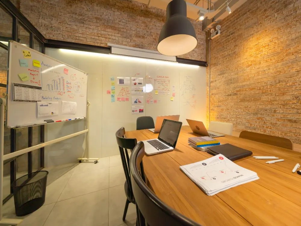 Sala de reunions amb portàtils, pissarres amb gràfics de marketing i paret de maó
