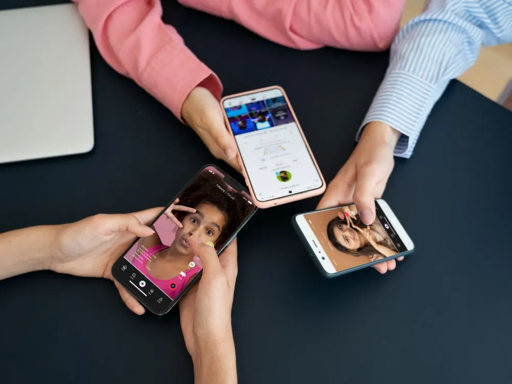 Tres personas sostienen móviles con vídeos y perfiles de redes sociales sobre una mesa