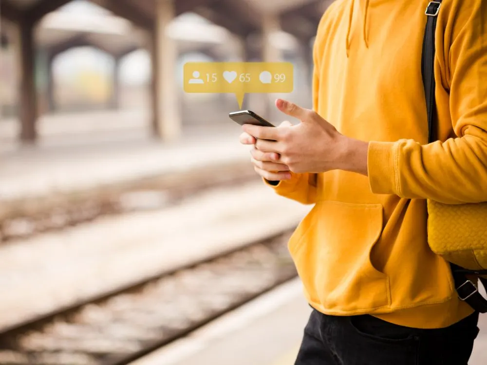 Joven con sudadera amarilla usa el móvil con notificaciones de seguidores, likes y comentarios