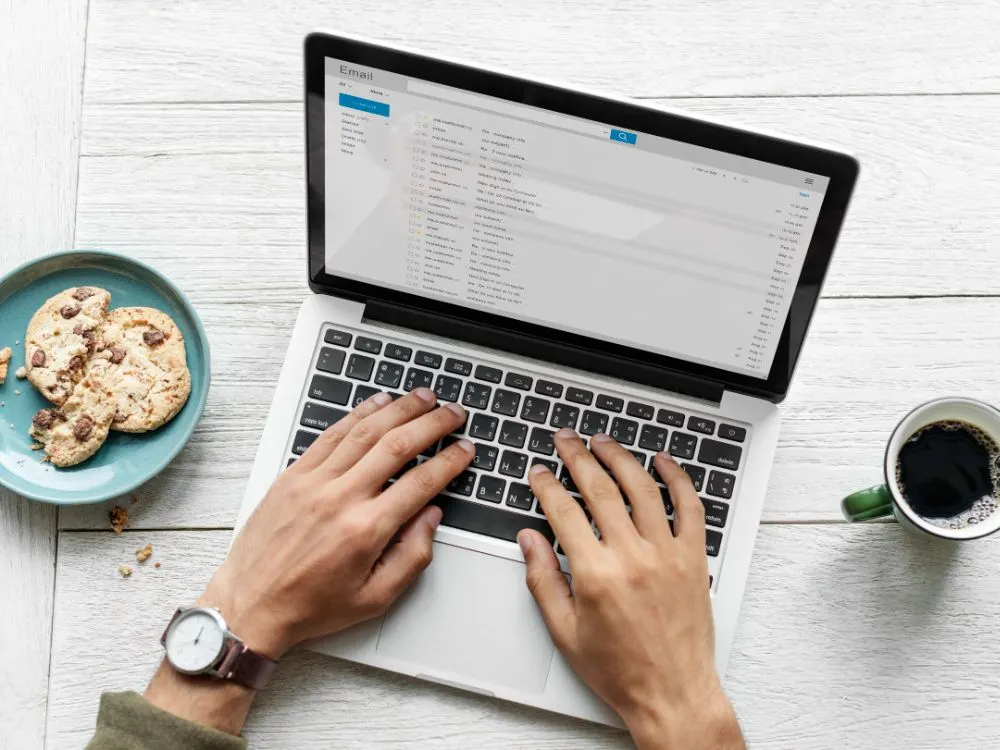 Manos escribiendo en un portátil con la bandeja de entrada del correo electrónico abierta