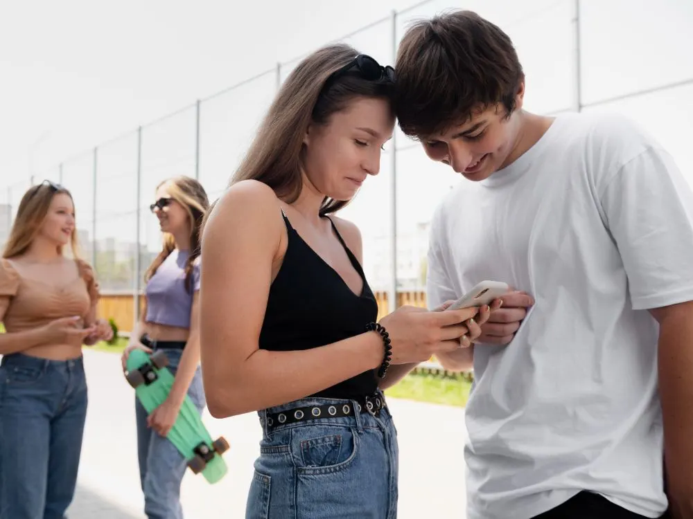 Parella d’adolescents mira un mòbil mentre dues noies amb un monopatí conversen darrere